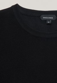 Czarny sweter wykonany na drutach z okrągłym dekoltem, z prążkowanym kołnierzem i metką. Uszyty z teksturowanej tkaniny, rozmiar medium widoczny na metce.