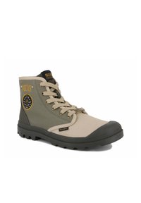 Bottes montantes beiges et olives avec tige en toile, capuchon en caoutchouc et semelle texturée. Présente un logo et un design circulaire sur le côté.