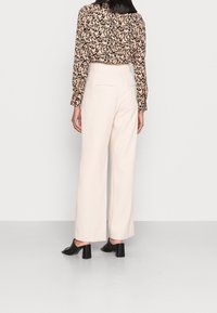 Světlé béžové kalhoty s širokými nohavicemi a hladkou texturou, s dvěma zadními kapsami, spárované s květinovým vzorem v černé a béžové blůze.