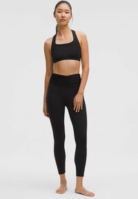 Fekete sportmelltartó és magas derekú leggings szett. A melltartón széles pántok és négyzet alakú kivágás található. A leggings derékrészén gathered részletek láthatók.