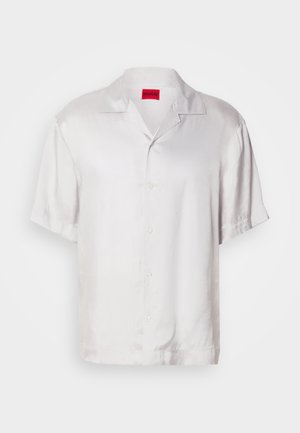 Bijela košulja kratkih rukava od glatkog materijala, s ovratnikom, zatvaranjem na dugmad i opuštenim krojem. Suptilni sjaj dodaje vizualni interes.