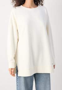 Kremowy, oversize'owy sweter z okrągłym dekoltem, długimi rękawami i prążkowanymi mankietami, wykonany z miękkiej, teksturowanej tkaniny.