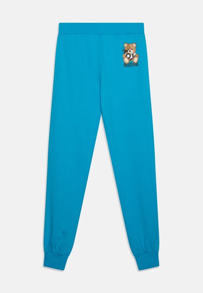 Pantalones de chándal turquesas hechos de tela suave, con una ilustración de un oso de peluche y el texto "MUSCHINO" en el muslo izquierdo.