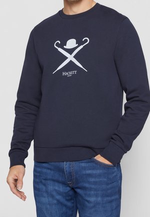 Sweatshirt bleu marine avec col rond, poignets et ourlet côtelés. Affiche un design graphique blanc de parapluies croisés et d'un chapeau melon, étiqueté "HACKETT."