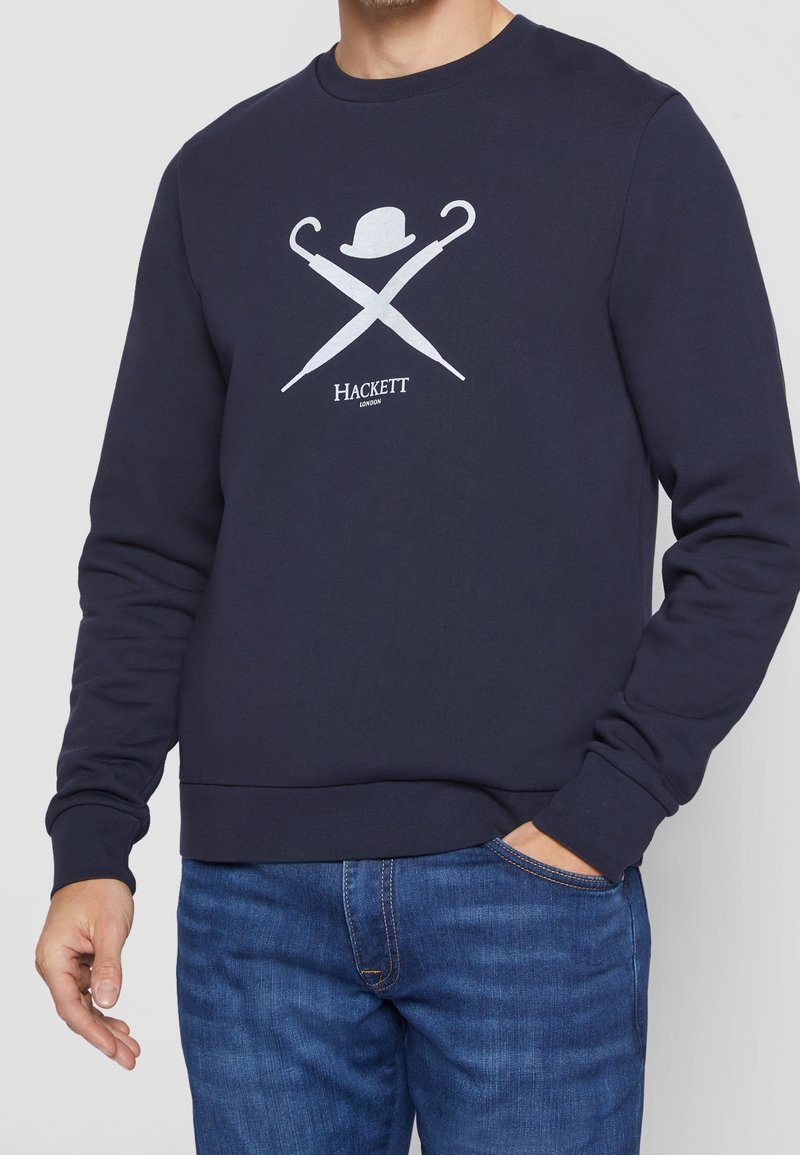 Felpa blu navy con collo a giro, polsini e orlo a coste. Presenta un design grafico bianco di ombrelli incrociati e un cappello bowler, contrassegnato con la scritta "HACKETT."
