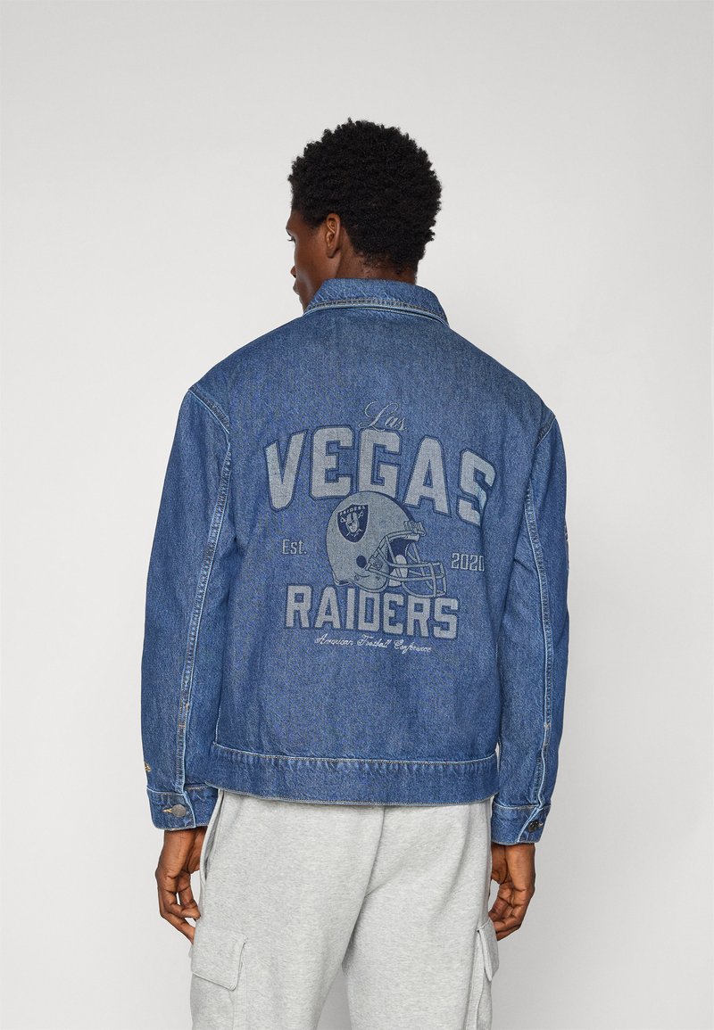 Veste en denim bleu foncé, arborant un graphisme "Las Vegas Raiders" au dos, avec un design de casque de football et des accents textuels.