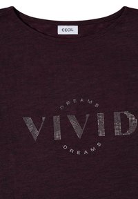 Dunkellila Shirt mit rundem Ausschnitt, "VIVID" in gepunkteten Buchstaben und den Worten "DREAMS" darüber und darunter in einem Kreis.