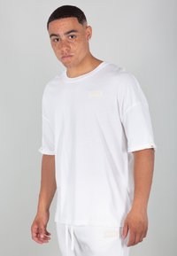 T-shirt bianco realizzato in morbido tessuto, con scollatura rotonda, maniche corte arrotolate e un'etichetta logo beige sul petto.