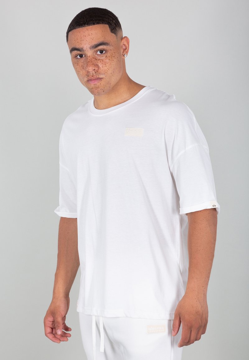 T-shirt bianco realizzato in morbido tessuto, con scollatura rotonda, maniche corte arrotolate e un'etichetta logo beige sul petto.