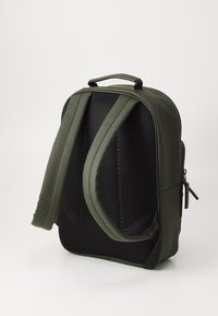 Sac à dos vert au design épuré, doté d'un dos en maille noire texturée, de bretelles rembourrées et d'une poche zippée sur le côté pour le rangement.