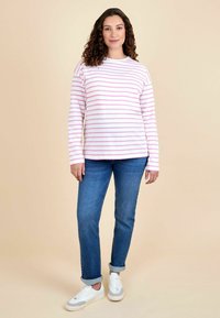 Langærmet stribet top i lyserød og hvid, parret med medium blå opkrøllede jeans og hvide sneakers med grå detaljer.