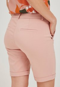 Rozā pielāgotie šorti ar gludu tekstūru, ar salocītu apdari un divām aizmugurējām kabatām. Dizains ir angels un pieguļošs.