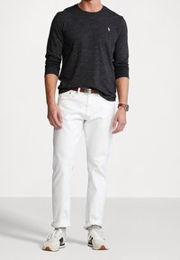 Dunkelgraues Langarmshirt, weiße Jeanshose, brauer Gürtel, grau-weiße Sneakers, präsentiert an einer stehenden Figur. Einfaches Design und Passform.