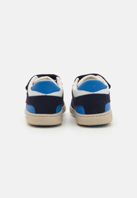 Baskets avec un corps en suedine bleu marine, des accents en cuir bleu, et une semelle en caoutchouc beige. Équipées de bandes Velcro pour un maintien sécurisé.