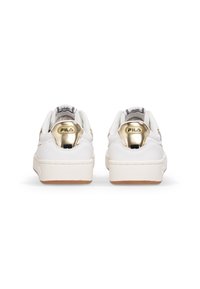Sneakers bianchi con un accento dorato sul tallone, tomaia in pelle texturizzata, colletto imbottito e suola in gomma. Logo Fila visibile sul tallone.