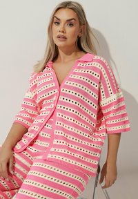 Completo lavorato a maglia rosa e crema con strisce orizzontali, dettagli a taglio, maniche corte e colletto con bottoni.