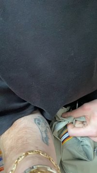 Person som har på seg en svart skjorte og lyse bukser med regnbuestripet belte; arm med gullarmbånd og synlig skalle-tatovering.