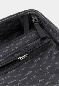 Zwarte stoffen tasinterieur met herhalend "GUESS" logo-patroon. Voorzien van een ritsvak en verstelbare banden voor organisatie.