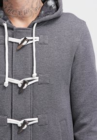 Graue Wolle-Mischung Kapuzenjacke mit Toggle-Verschlüssen, weißen Zugbändern und einem gemusterten Futter. Enthält seitliche Taschen und strukturierte Stoffe.