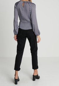 Blus med lång ärm i mönstrad marinblå och vit tyg, med en nyckelhålsdetalj baktill. Kombinerad med svarta byxor med uppvikt ärmslut och klackskor.