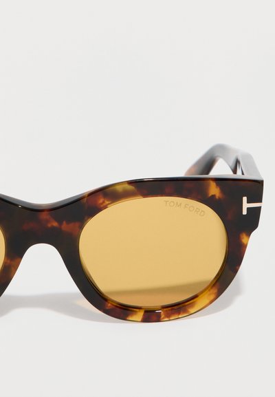 Γυαλιά ηλίου με σκελετό σε χρώμα χελώνας και φακούς κεχριμπαριού, με διακριτικό λογότυπο "Tom Ford" στον φακό και το λογότυπο "T" στον βραχίονα.