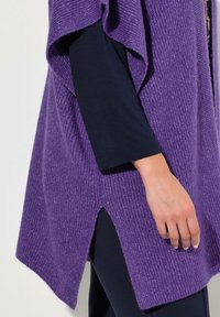 Lila stickad poncho med ribbat mönster, med sidslitsar. Kombinerad med en figurnära marinblå långärmad topp.