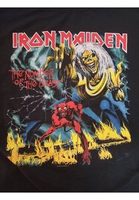 Černé tričko s grafickým designem kosterní postavy a červeného ďábla na ohnivém pozadí, se texty "IRON MAIDEN" a "THE NUMBER OF THE BEAST".