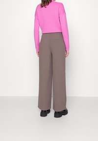 Růžový pletený svetr s dlouhými rukávy ve slim fit stylu, doplněný hnědými širokými kalhotami. Kalhoty mají zadní kapsu a elastický pas.
