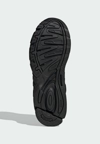 Semelle de chaussure de sport noire avec une surface en caoutchouc texturé, des motifs de traction, des accents circulaires et une zone de talon renforcée.