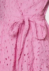 Růžové šaty s broderie anglaise vzorem. Mají texturovanou tkaninu, nařasený pas a zavírání na boku s tkaničkou.