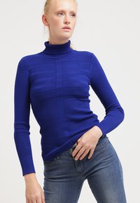 Königblauer Rollkragenpullover mit gerippter Textur und horizontalen Streifendetails. Schmaler Schnitt, lange Ärmel und flacher Kragen.