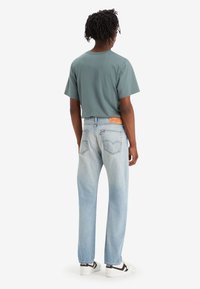 Blå denimjeans med avslappnad passform och blekt utseende, kombinerat med en grå t-shirt med kort ärm. Synlig märkesläderlapp på baksidan.