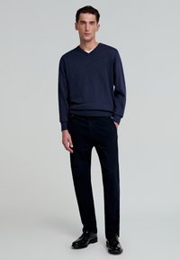 Pulover marin cu guler în V și mâneci lungi, asociat cu pantaloni închiși la culoare și pantofi negri. Design simplu cu o finisare texturată, fără modele vizibile.