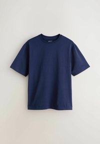 T-shirt en coton bleu marine à manches courtes suspendu contre un mur clair uni, avec un col rond et une coupe décontractée.