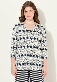 Blouse à col en V avec des manches trois-quarts, arborant un motif de coquillage bleu marine et blanc sur un fond clair, fabriquée en tissu doux et léger.