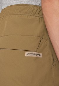 Khaki kratke hlače iz lahkega materiala, s klasičnim pasom, stranskimi žepi in obližem z logotipom. Preprosto šivanje in teksturne podrobnosti.