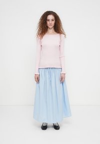 Ροζ κορυφή με μακριά μανίκια και ριμπ ύφανση, σε συνδυασμό με φούστα σε ανοιχτό γαλάζιο χρώμα, με ελαστική μέση και μήκος μέχρι τον αστράγαλο. Μαύρα επίπεδα παπούτσια ολοκληρώνουν το σύνολο.