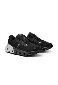 Des chaussures de sport noires avec un dessus en maille respirante, une semelle rembourrée avec de plus grands trous et des accents blancs contrastants sur la semelle intermédiaire.