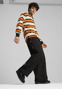Striped long-sleeve shirt in orange and cream, paired with black wide-leg pants featuring logo accents and black sneakers with teal soles.