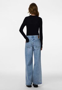 Svart ribbad långärmad topp kombinerad med ljusblå vida jeans med bakficka och två bakfickor, mot en enfärgad bakgrund.