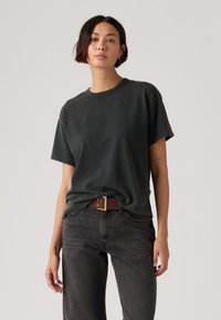 Σκούρο γκρι βαμβακερό T-shirt με άνετη εφαρμογή, στρογγυλή λαιμόκοψη, κοντά μανίκια, σε συνδυασμό με μαύρα τζιν και καφέ ζώνη με χρυσή πόρπη.