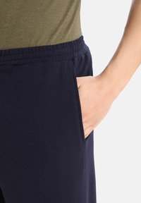 Mörkblå joggers har en elastisk midja och en sidficka. Materialet verkar mjukt och lätt, med en slät yta.