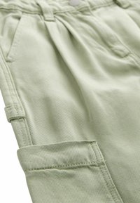 Pantaloni di cotone verde chiaro con una trama a coste, dotati di tasche laterali, chiusura con bottone e orli arrotolati.