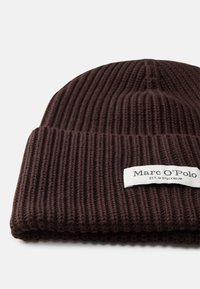 Gorro marrón de punto con textura de canalé y una etiqueta blanca que dice "Marc O'Polo" y "EST. EN STOCKHOLM."