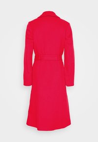 Long manteau en laine rouge avec un large col et une ceinture assortie, vu de dos sur un fond clair uni.