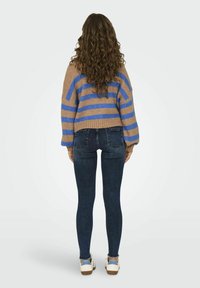 Maglione a righe marrone e blu con maniche oversize, abbinato a jeans skinny in denim scuri e sneakers bianche con dettagli blu.