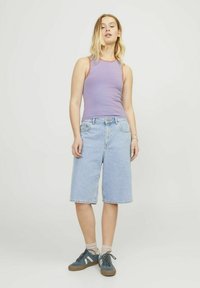 Top sin mangas lila con acentos rojos, combinado con pantalones cortos de mezclilla azul claro. El modelo lleva zapatillas en color verde azulado y calcetines color marrón claro. Atuendo sencillo y casual.