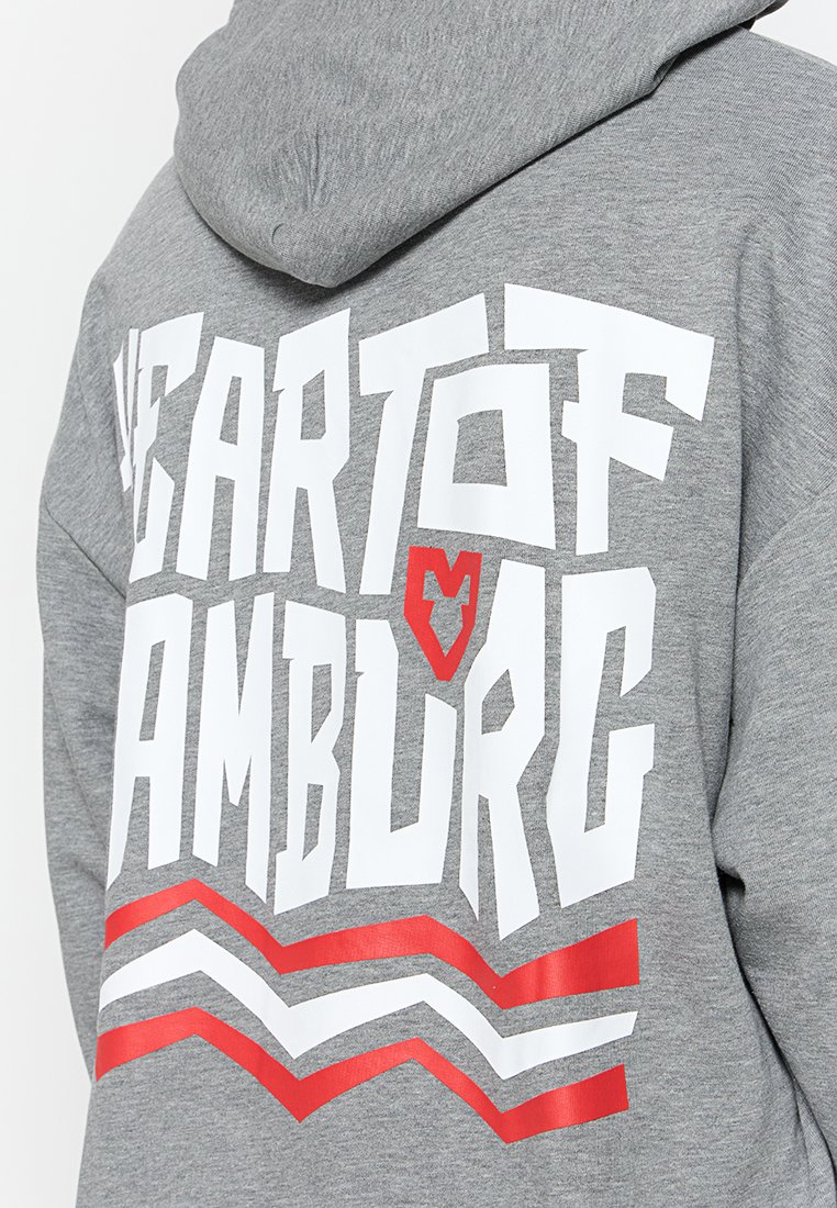 Sudadera gris con texto en blanco y rojo en un estilo audaz que dice "HEART OF HAMBURG" acompañado de un gráfico de corazón, y franjas en forma de chevron rojas en el dobladillo.