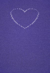 Fialová látka s texturovaným pleteným vzorem, který obsahuje design ve tvaru srdce vytvořený z malých bílých kruhových výřezů.