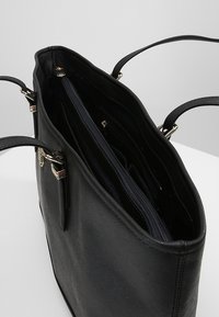 Černá kožená kabelka s dvojitými rukojeťmi, horním zipem a vnitřní kapsou na zip, zobrazená otevřená na bílé ploše.